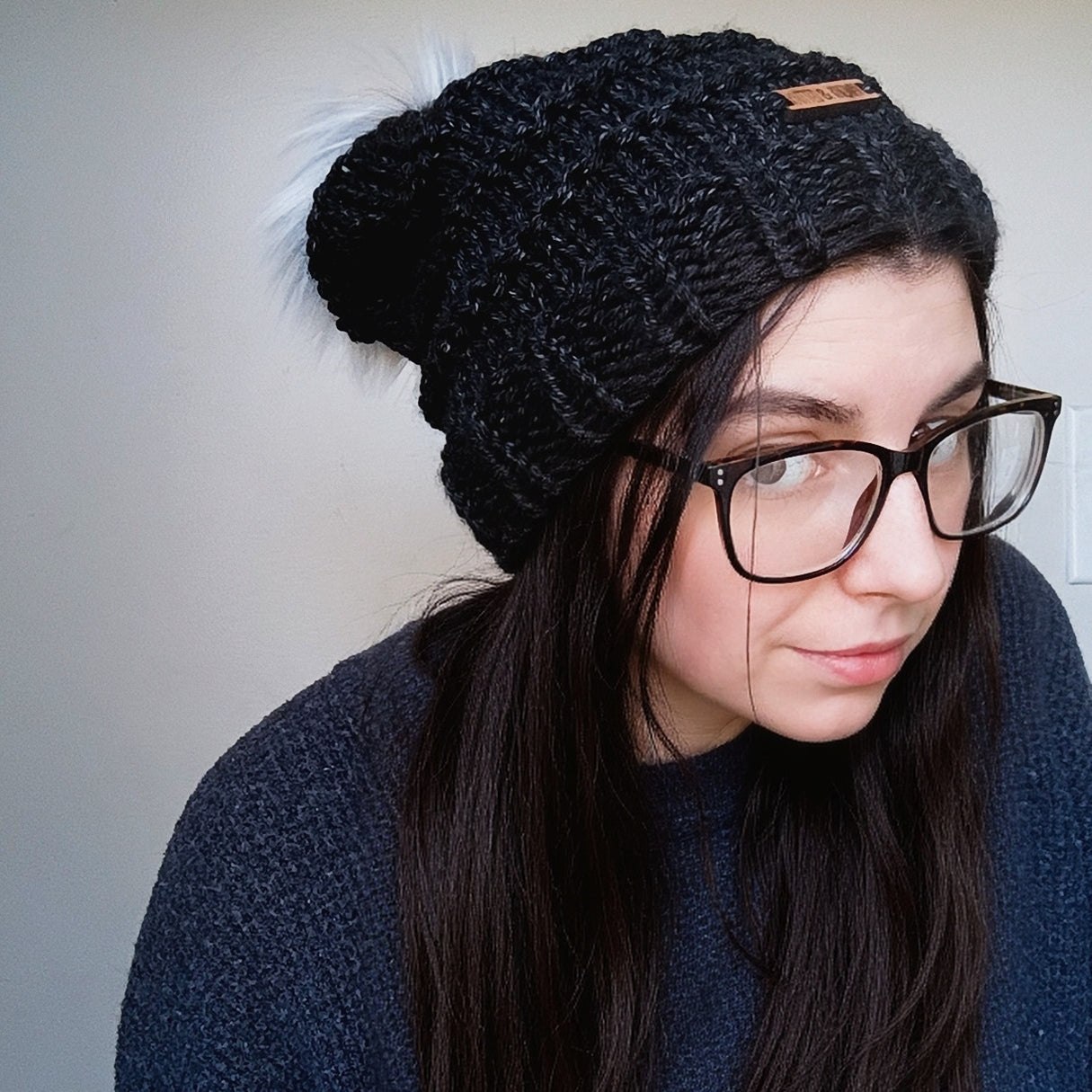 Person wearing a black knitted slouchy beanie and glasses against a plain background