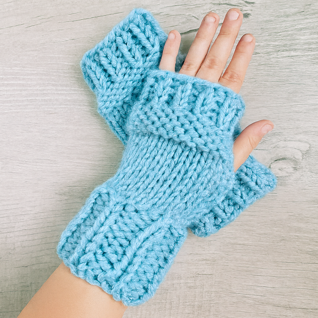 Blue knitted fingerless gloves on a light wooden surface