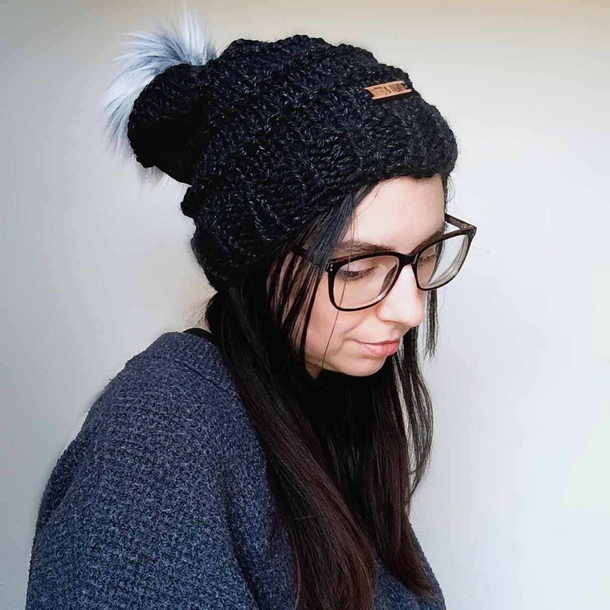 Person wearing a black knit beanie with a pom-pom on a plain background