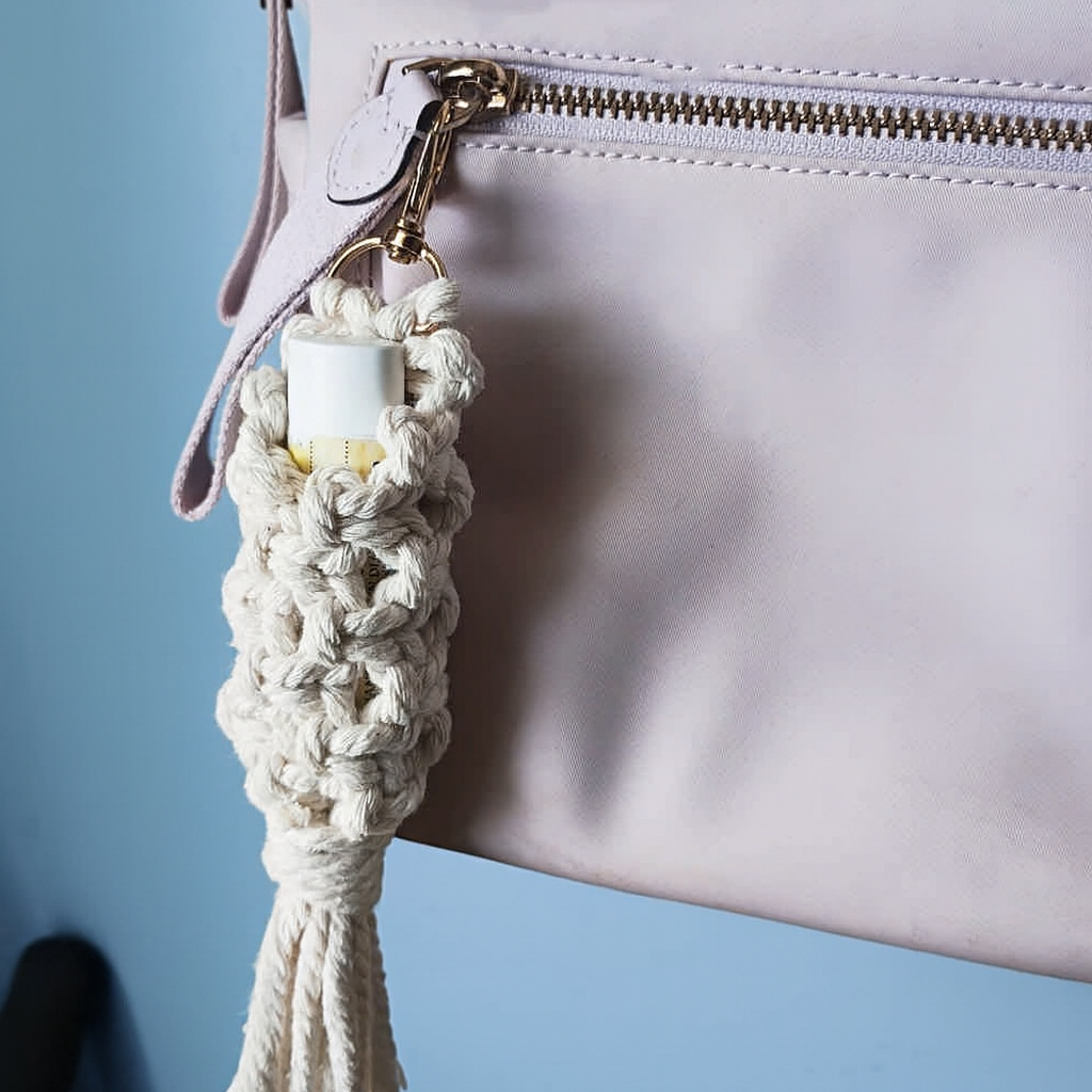Close-up of a beige macrame keychain attached to a light pink handbag on a blue background