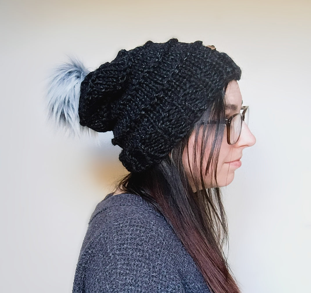 Person wearing a black knit beanie with a pom-pom on a plain background